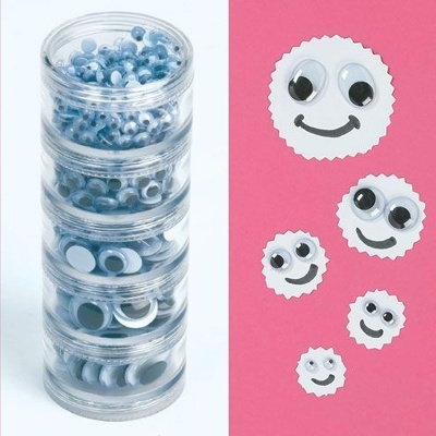 Olhos móveis de plástico em recipientes transparentes empilhados junto de rostos sorridentes feitos com papel e olhos móveis.