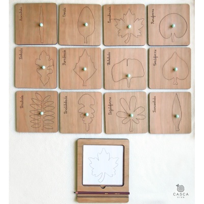 Painéis de madeira com desenhos de folhas e nomes, com puxadores brancos, sobre parede branca, e suporte de madeira com papel desenhado.