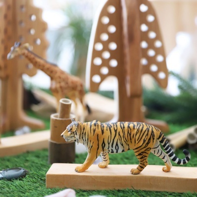 Figuras de brinquedo de tigre e girafa num cenário de madeira e relva artificial