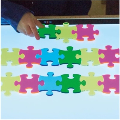 Criança montando peças de puzzle coloridas grandes sobre mesa iluminada