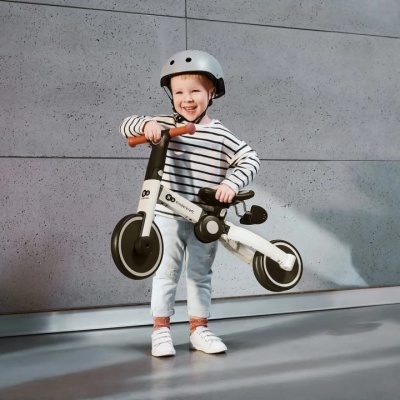 Criança segurando bicicleta de equilíbrio branca e preta com capacete.