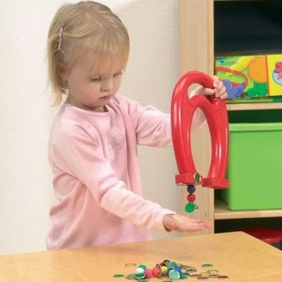 Menina loira com camisola rosa a segurar imã vermelho em forma de ferradura sobre mesa com chapas coloridas