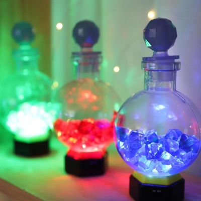 Frascos de vidro redondos com cristais iluminados em azul, vermelho e verde numa superfície de madeira