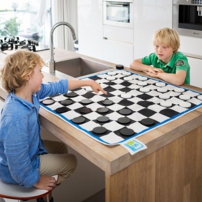 Tabuleiro de jogo de damas gigante numa bancada de cozinha com duas crianças a jogar