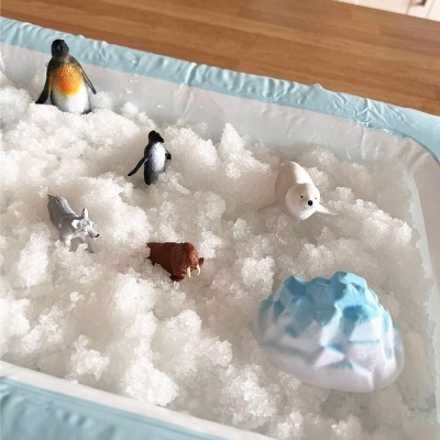 Miniaturas de animais polares e iglu em neve artificial numa caixa azul clara