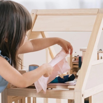 Criança a brincar com casa de bonecas em madeira clara e tecidos rosa