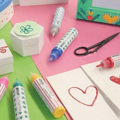 Canetas para tecido coloridas, caixas decorativas, tesoura preta e papel com corações desenhados sobre mesa colorida