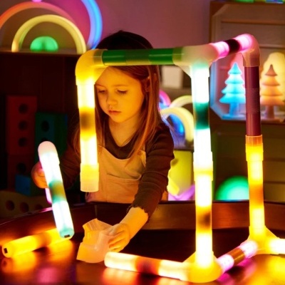 Criança a brincar com tubos luminosos coloridos e montar estruturas em ambiente interior