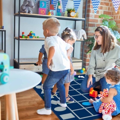 Tapete de brincar azul escuro com padrão geométrico, crianças e mulher num ambiente de brincadeira