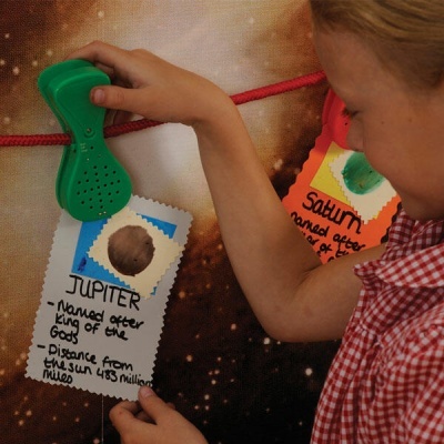 Cartões informativos sobre planetas Júpiter e Saturno presos por clipes verdes a um fio num fundo espacial.