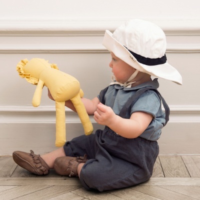 Bebé sentado segurando brinquedo de peluche amarelo em fundo de parede branca e chão de madeira