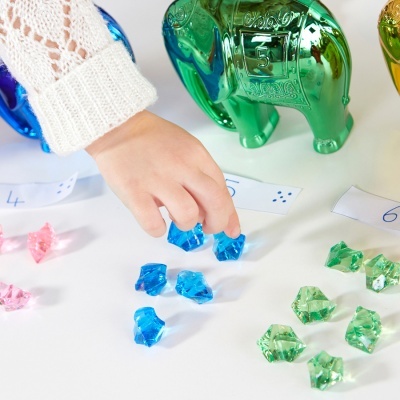 Mão de criança a pegar peças de jogo azuis com elefantes de vidro colorido ao fundo