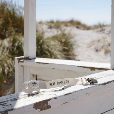 Chupeta branca com suporte de tecido branco com texto em ingles sobre madeira branca desgastada na praia