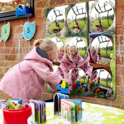 Painel de nove espelhos redondos na parede refletindo criança a brincar com blocos de construção