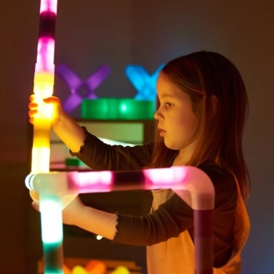Menina a montar tubos plásticos iluminados coloridos em ambiente interior escuro