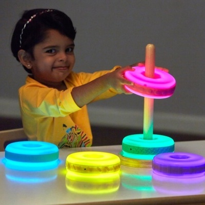 Criança a brincar com brinquedo empilhável de anéis luminosos coloridos em madeira.
