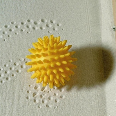 Bola amarela pontiaguda sobre tecido branco com padrão em relevo e estrutura de madeira com aro vermelho