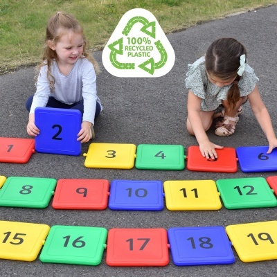 Peças quadradas de plástico coloridas numeradas de 1 a 20 no chão com crianças a brincar