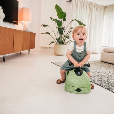 Criança sentada em brinquedo verde numa sala moderna com decoração clara e plantas