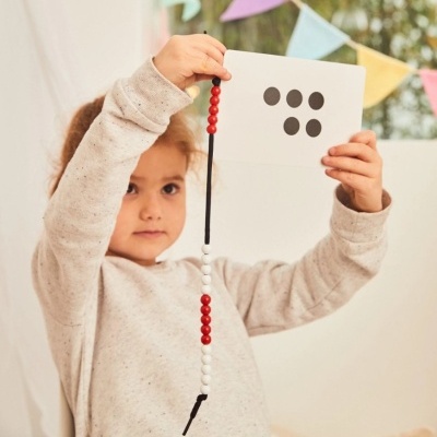 Criança com contas vermelhas e brancas e cartão com pontos pretos