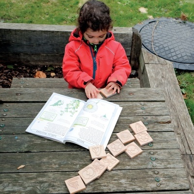 Criança lendo livro ao ar livre com blocos de madeira gravados em mesa de madeira.