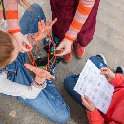 Três crianças sentadas a jogar com fio colorido e seguir instruções numa folha