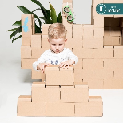 criança a empilhar blocos de cartão castanho com planta ao fundo