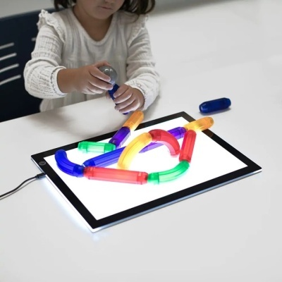 Criança a brincar com tubos flexíveis coloridos sobre tablet iluminado.