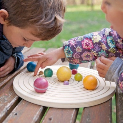Brinquedo de madeira do sistema solar com planetas coloridos e crianças a brincar ao ar livre
