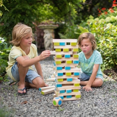 Duas crianças jogando jogo de blocos de madeira coloridos ao ar livre em superfície de pedras.