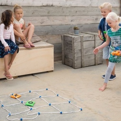 Cinco crianças a jogar em área de areia com banco de madeira clara e jogo de rede colorido no chão