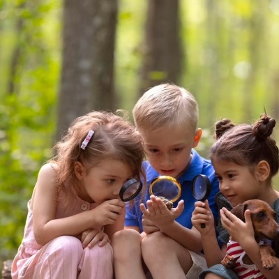 Três crianças ao ar livre numa floresta com lupas e um cão pequeno