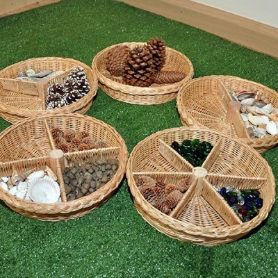 Cinco cestos redondos de vime com vários elementos naturais e bolas de vidro sobre relva artificial