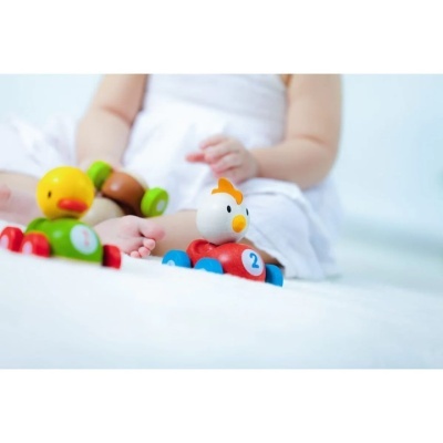 Brinquedos de madeira de pato e galinha em carrinhos coloridos com números, criança ao fundo