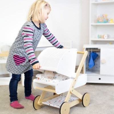 Menina brincando com berço de madeira e tecido em quarto de crianças