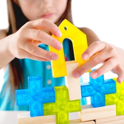 Mãos de criança a montar peças de jogo de construção coloridas e blocos de madeira.