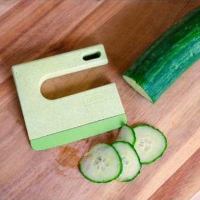 Cortador manual de legumes com pepino fatiado em tábua de madeira