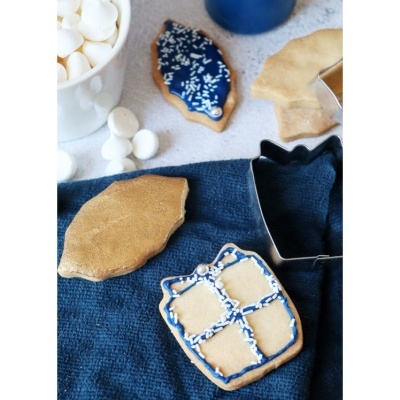 Biscoitos decorados em cima de pano azul com cortadores de biscoito e tigela branca ao fundo
