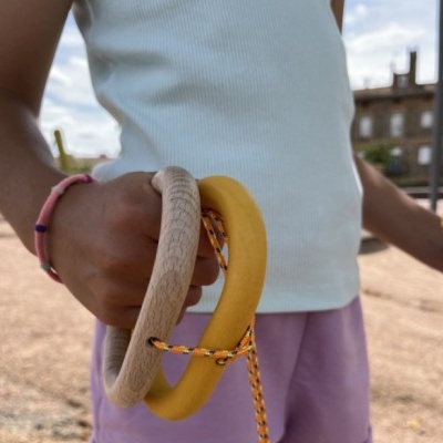 Anéis de madeira e silicone com cordão segurados por criança com roupa clara ao ar livre