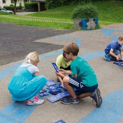 Crianças a jogar com placas azuis com letras no chão de um parque