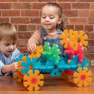 Crianças a brincar com blocos construíveis coloridos em mesa de madeira, fundo parede tijolos.