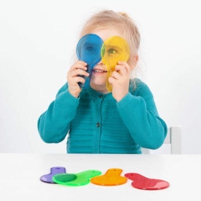 Criança com lentes coloridas de plástico nas mãos e outras sobre mesa branca