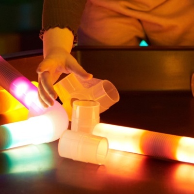 Braço de criança a tocar tubos luminosos coloridos sobre mesa preta