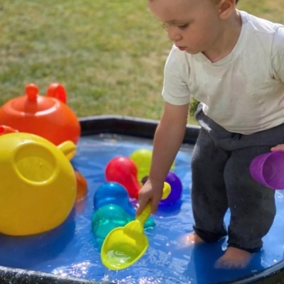Criança pequena brincando com brinquedos de água coloridos em tabuleiro azul ao ar livre