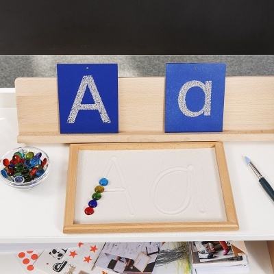 Mesa com tabuleiro de letras em relevo, botões coloridos e cartões azuis com letras A