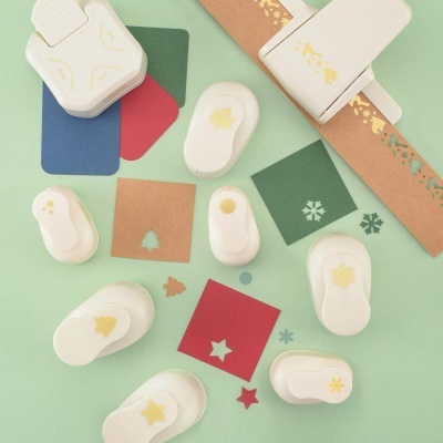 Furadores de papel brancos com motivos natalícios sobre papéis coloridos e pedaços furados.