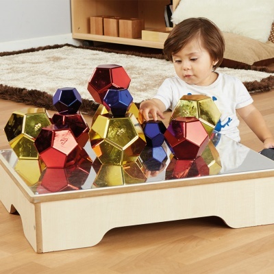Criança brinca com blocos magnéticos coloridos sobre mesa espelhada
