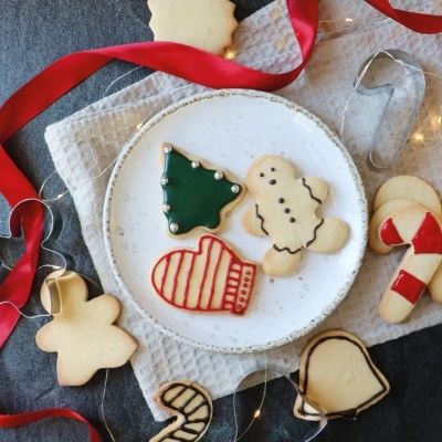 Biscoitos decorados de Natal sobre prato branco e pano bege com fita vermelha
