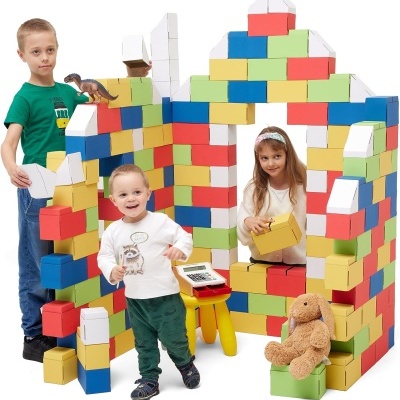 Três crianças brincam com blocos de construção grandes coloridos formando uma casa