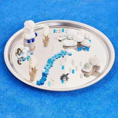 Tabuleiro redondo metálico espelhado com pequenas esculturas e pedras coloridas